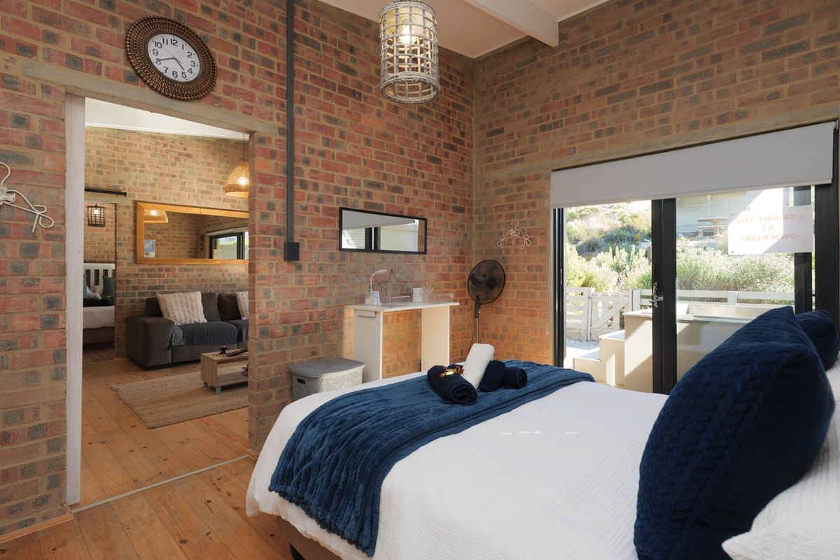 A rustic bedroom featuring exposed brick walls, timber flooring, and sliding glass doors that provide direct access to an outdoor area.
