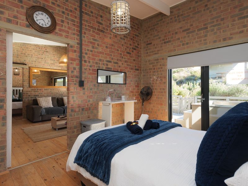 A rustic bedroom featuring exposed brick walls, timber flooring, and sliding glass doors that provide direct access to an outdoor area.