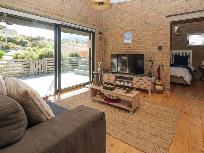 A cozy living room featuring exposed brick walls, timber flooring, and large sliding glass doors that provide seamless access to the outdoor patio area.