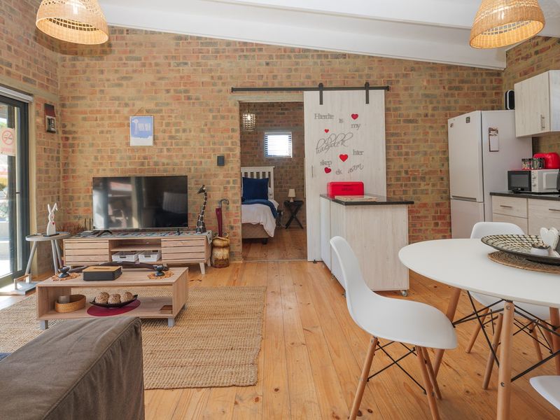 Open-plan living area featuring exposed brick walls, timber flooring, and a functional kitchen, with direct access to an outdoor patio through sliding glass doors.