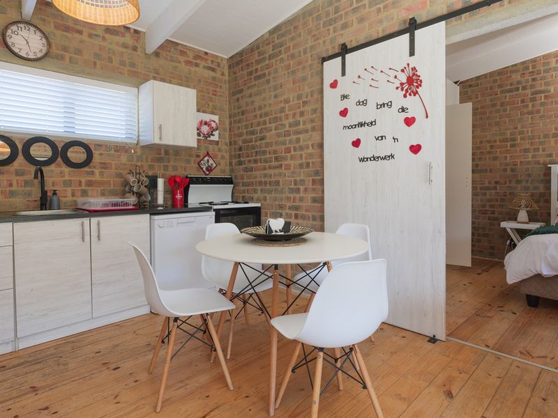 Open-plan living area featuring exposed brick walls, timber flooring, and a compact kitchen with a sliding barn door leading to the bedroom.