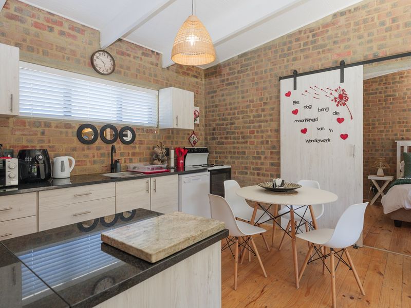 Open-plan kitchen and living area featuring exposed brick walls, timber flooring, and a sliding barn door leading to an adjacent bedroom.