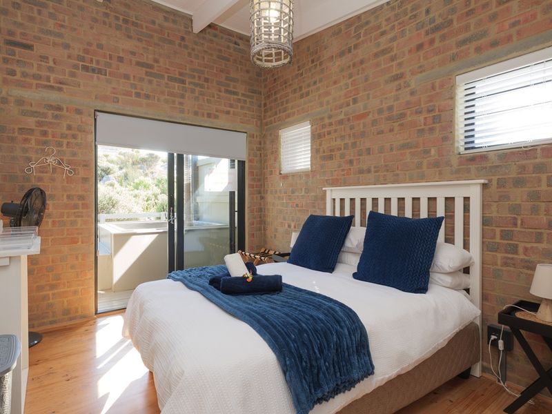 A cozy bedroom featuring exposed brick walls, timber flooring, and a sliding glass door providing access to an outdoor area.