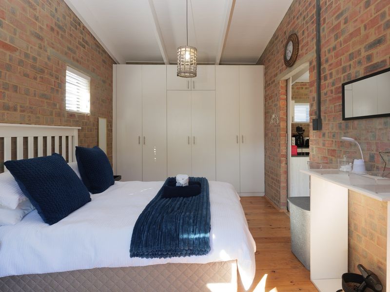 A well-maintained bedroom featuring exposed brick walls, timber flooring, exposed beam ceilings, and ample built-in cupboard storage.