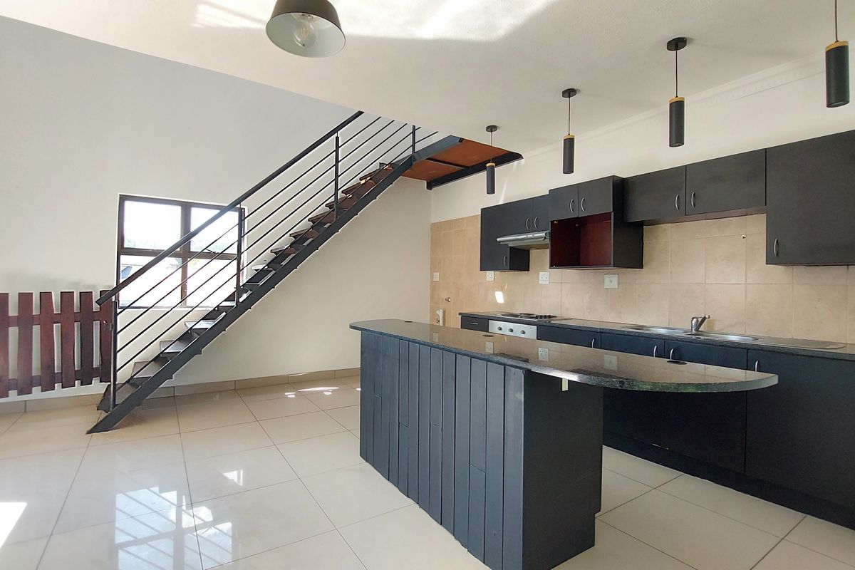 Open-plan kitchen and living area featuring dark cabinetry, granite countertops, a breakfast island, and a staircase leading to the upper level.