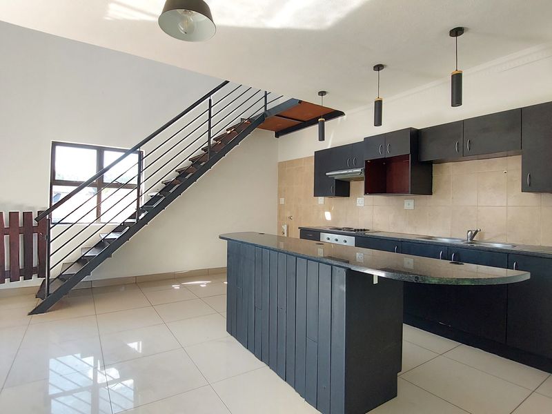 Open-plan kitchen and living area featuring dark cabinetry, granite countertops, a breakfast island, and a staircase leading to the upper level.
