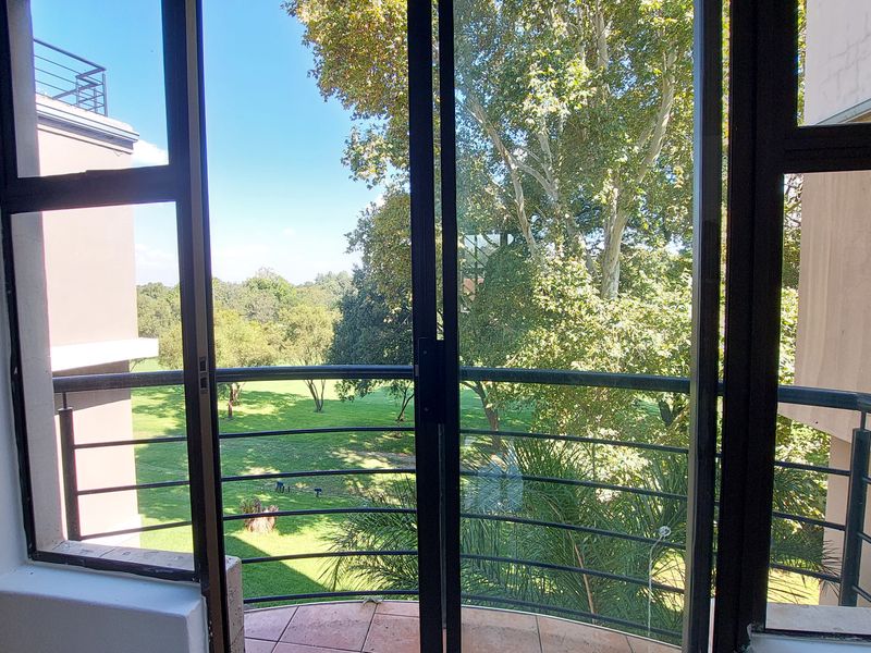 A private balcony featuring tiled flooring and metal railings, offering a pleasant view of the surrounding green landscape and trees.