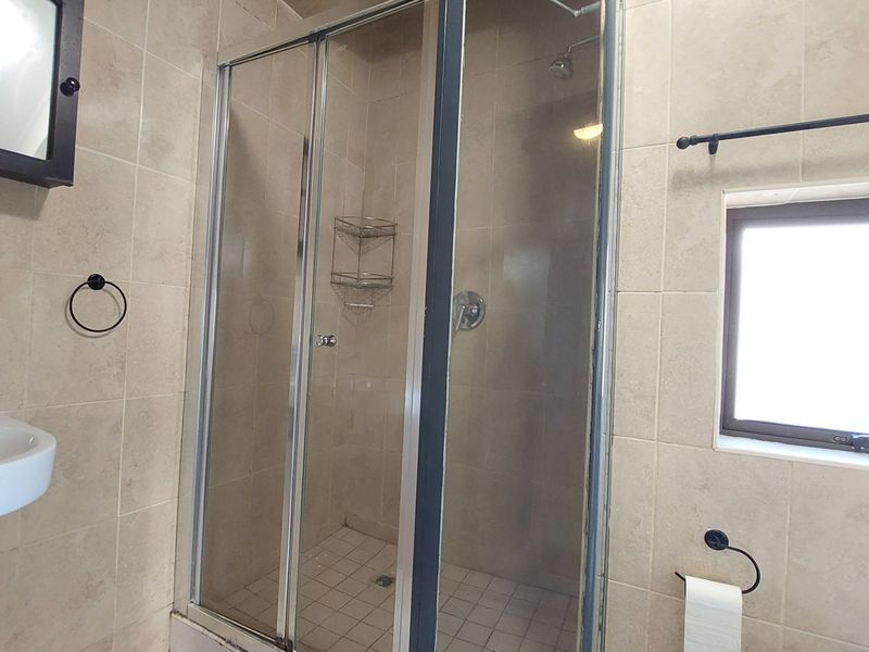 A functional bathroom featuring a tiled shower enclosure, wall-mounted basin, and neutral wall tiling, providing a clean and practical space.