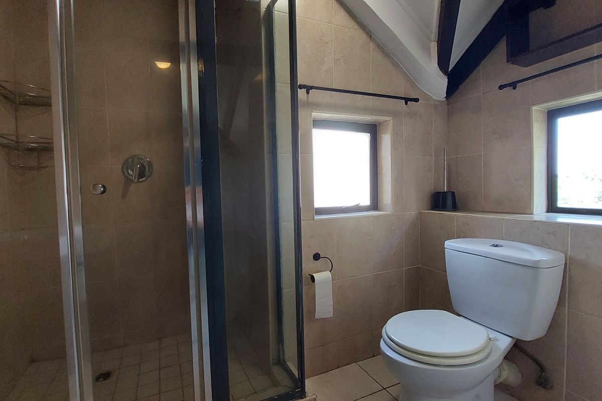 A functional bathroom featuring a shower enclosure, toilet, tiled finishes, and exposed timber beams under a pitched ceiling.