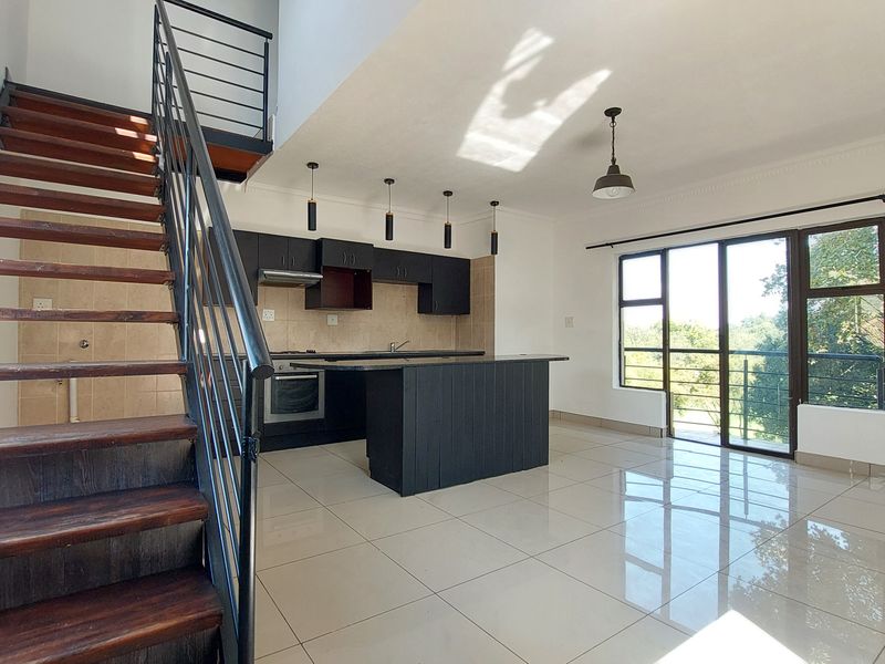 Spacious open-plan living area featuring a modern kitchen with dark cabinetry, a central island, tiled floors, and a staircase leading to an upper level.