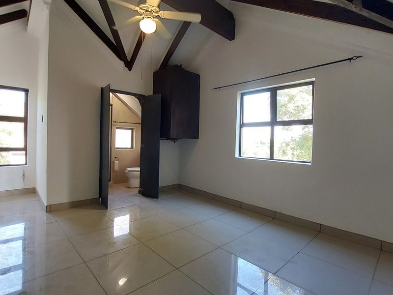 Spacious bedroom featuring vaulted ceilings with exposed timber beams, tiled flooring, and an en-suite bathroom access.