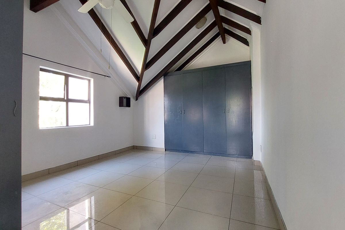 Spacious bedroom featuring vaulted ceilings with exposed timber beams, tiled flooring, and ample built-in cupboard storage.