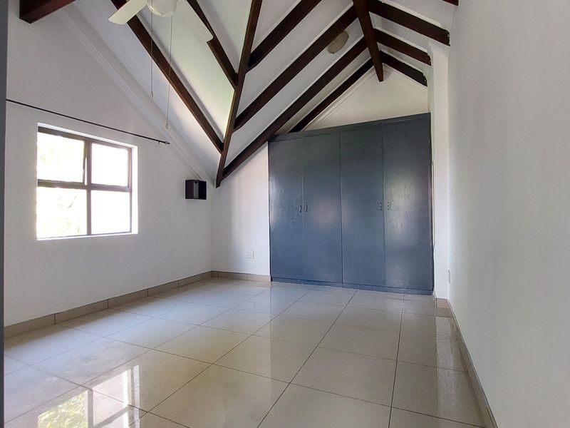 Spacious bedroom featuring vaulted ceilings with exposed timber beams, tiled flooring, and ample built-in cupboard storage.