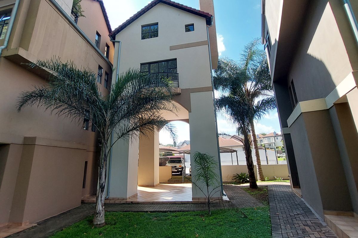 Rear view of the apartment building featuring a covered patio area, paved walkways, and a small balcony on the upper level.