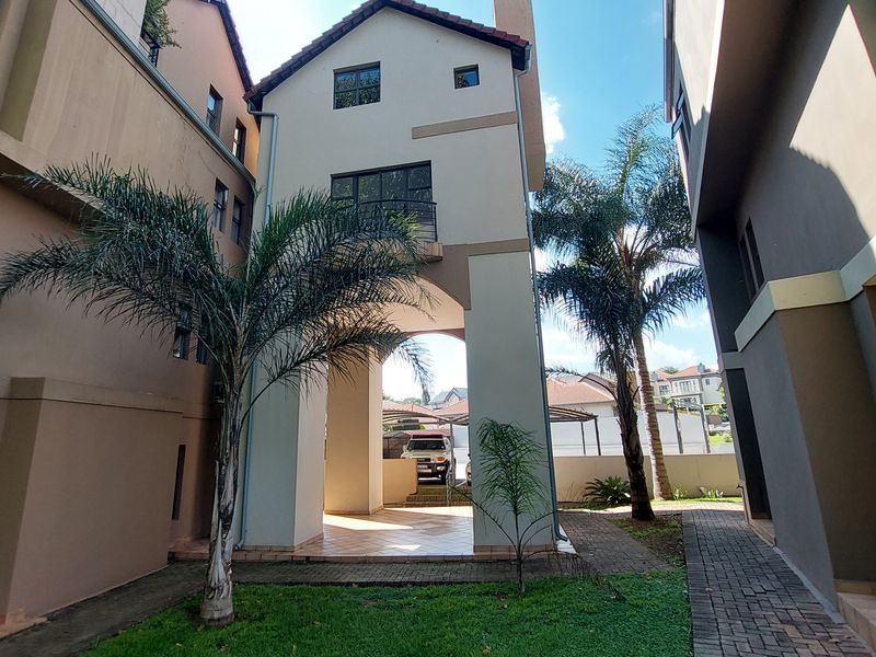 Rear view of the apartment building featuring a covered patio area, paved walkways, and a small balcony on the upper level.