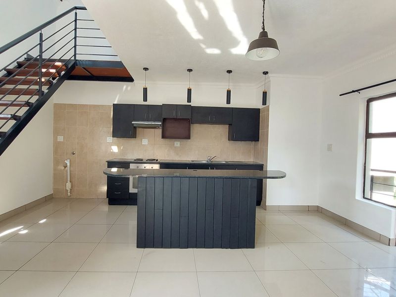 Open-plan kitchen and living area featuring dark cabinetry, a central island, tiled flooring, and a modern staircase leading to the upper level.