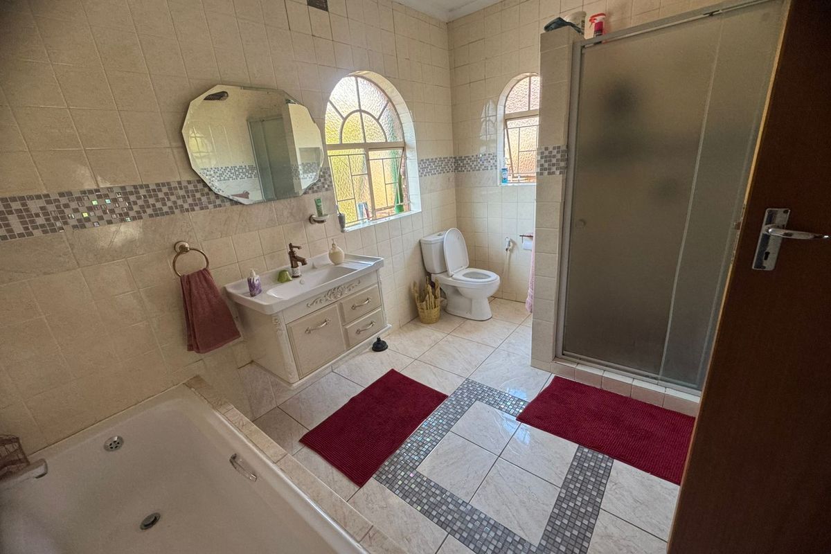 A dated bathroom featuring a built-in vanity, shower enclosure, bathtub, and toilet, finished with tiled walls and flooring and arched windows.