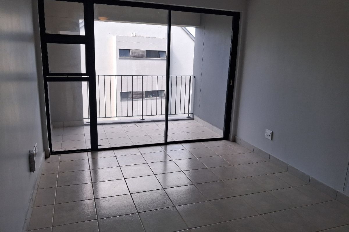An empty living area featuring tiled flooring and large sliding glass doors that open onto a private balcony.
