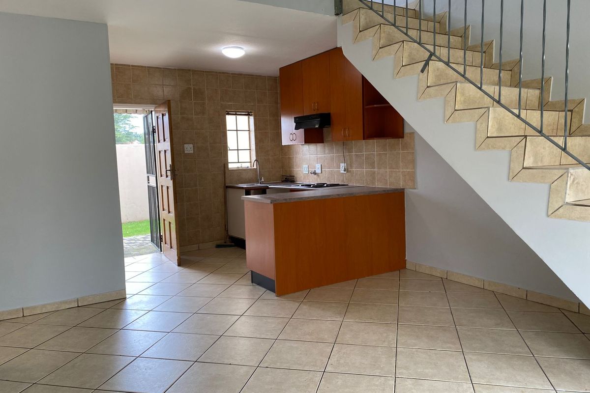 Compact kitchen featuring built-in wooden cabinetry, tiled backsplash, and a breakfast counter, conveniently located under the staircase with direct access to the exterior.