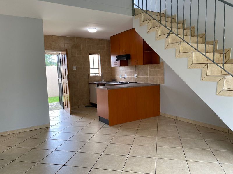 Compact kitchen featuring built-in wooden cabinetry, tiled backsplash, and a breakfast counter, conveniently located under the staircase with direct access to the exterior.