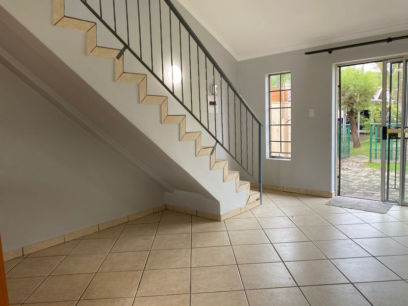 Bright entrance area featuring tiled flooring, a staircase with a metal balustrade, and direct access to the garden through a glass door.