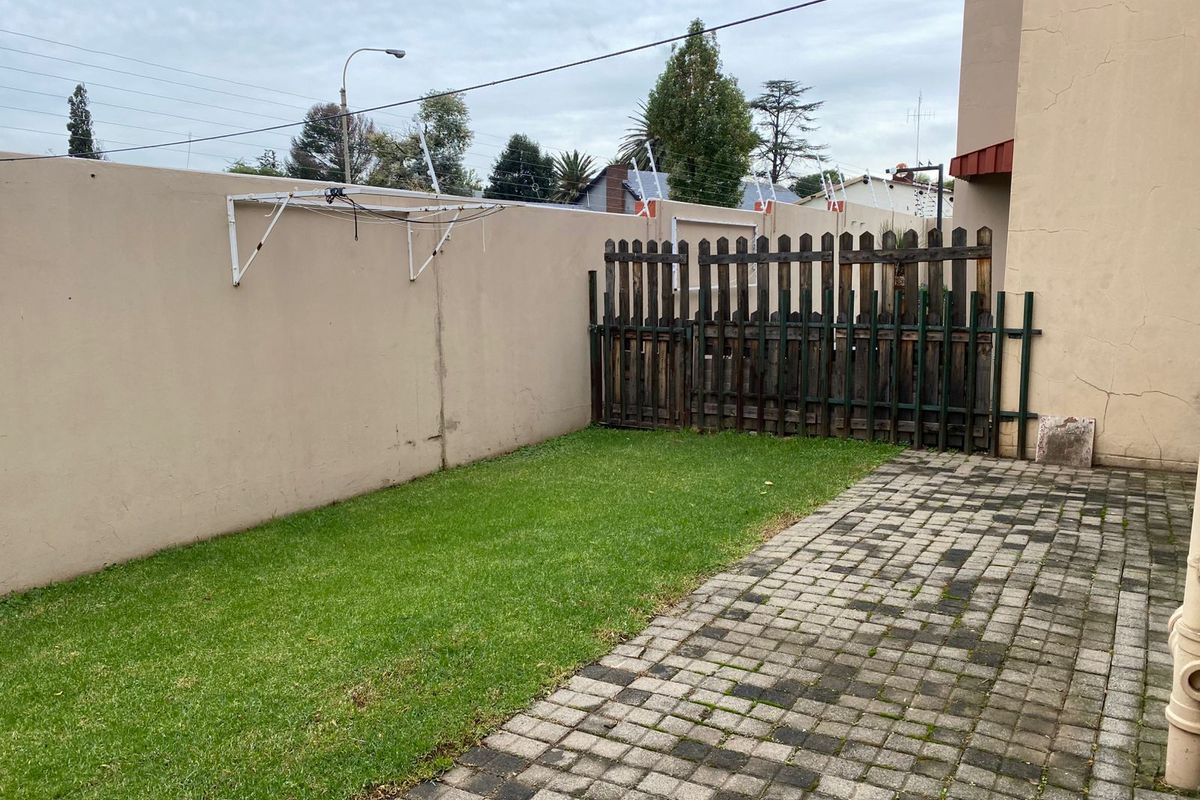 A private rear courtyard featuring a paved patio area, a small lawn, and a boundary wall with a mounted clothesline.