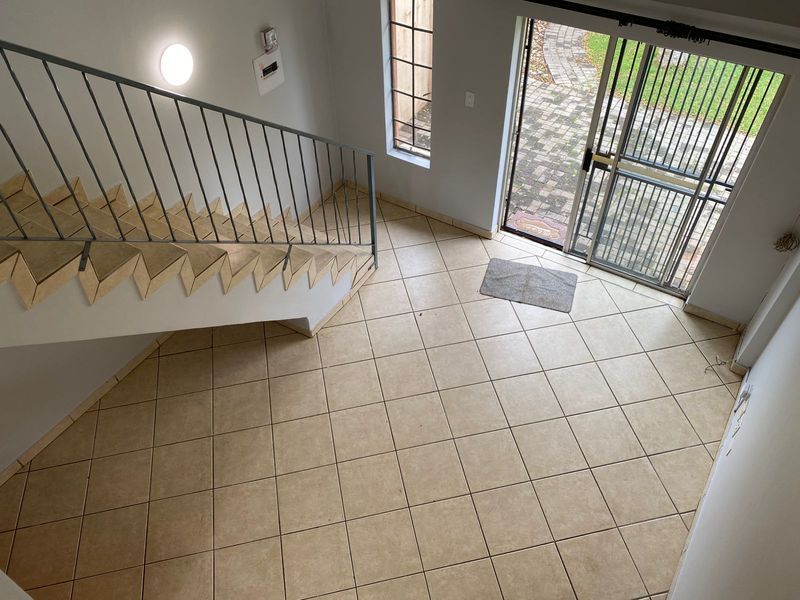 An open-plan entrance area featuring tiled flooring, a metal staircase railing, and direct access to the exterior through a security gate and sliding door.