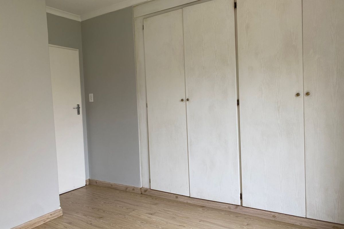 A clean, empty bedroom featuring neutral grey walls, light wood-look laminate flooring, and ample built-in cupboard storage.