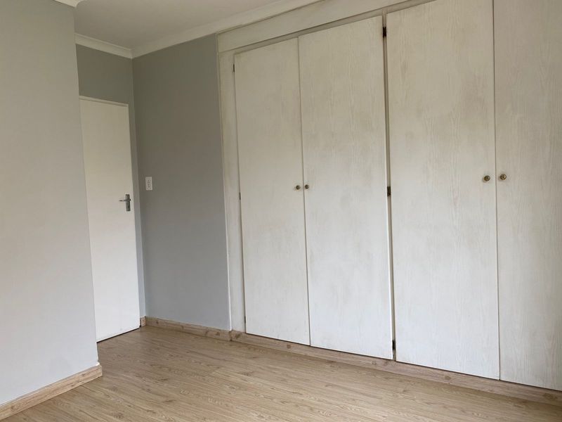 A clean, empty bedroom featuring neutral grey walls, light wood-look laminate flooring, and ample built-in cupboard storage.