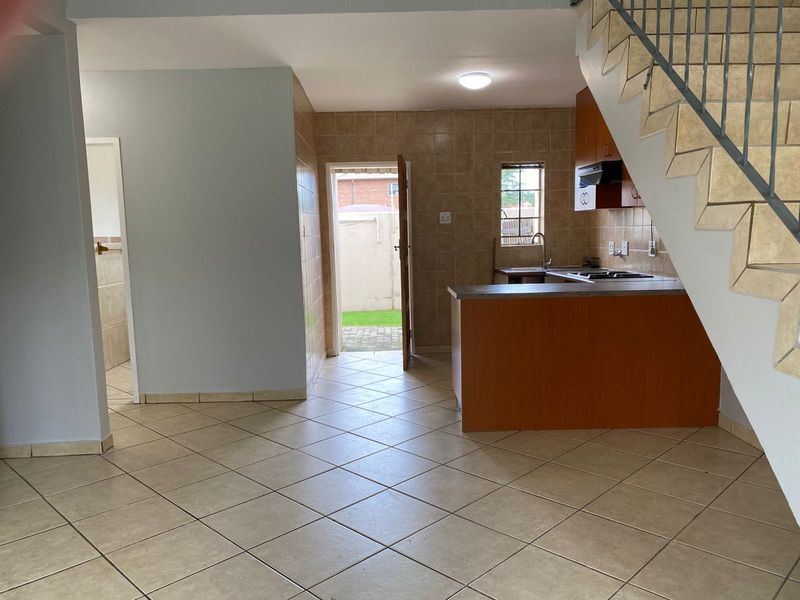 Open-plan kitchen and living area featuring tiled flooring, built-in cabinetry, and a staircase, with direct access to the rear exterior.