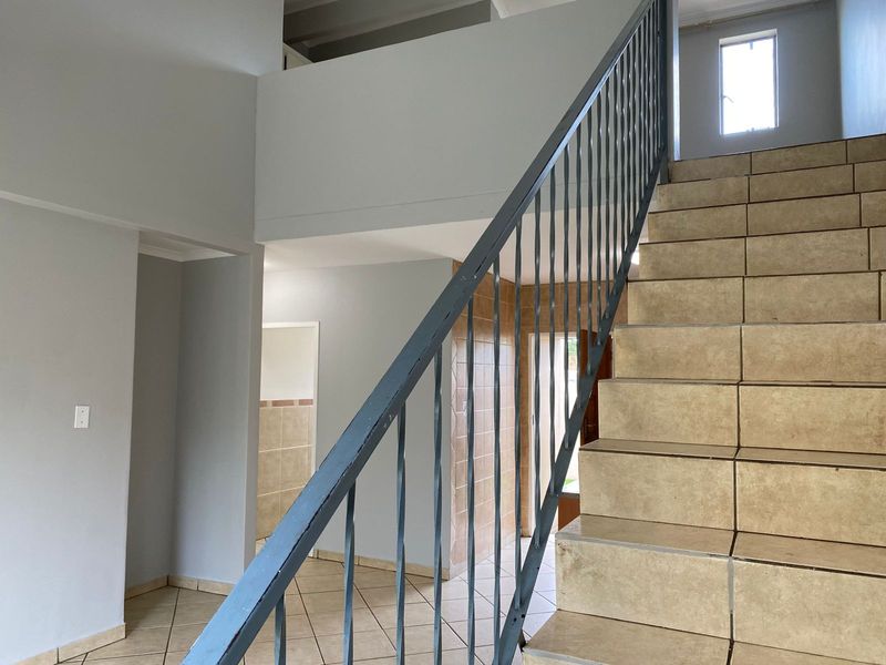 An open-plan entrance area featuring a tiled staircase with a metal balustrade, leading to an upper level with neutral wall finishes.
