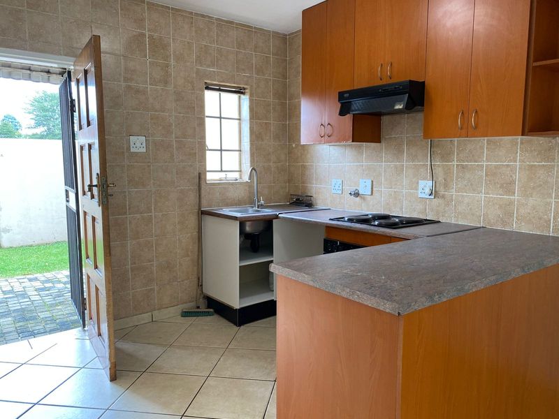 A functional kitchen featuring laminate cabinetry, a built-in electric hob with extractor fan, and direct access to the outdoor area.