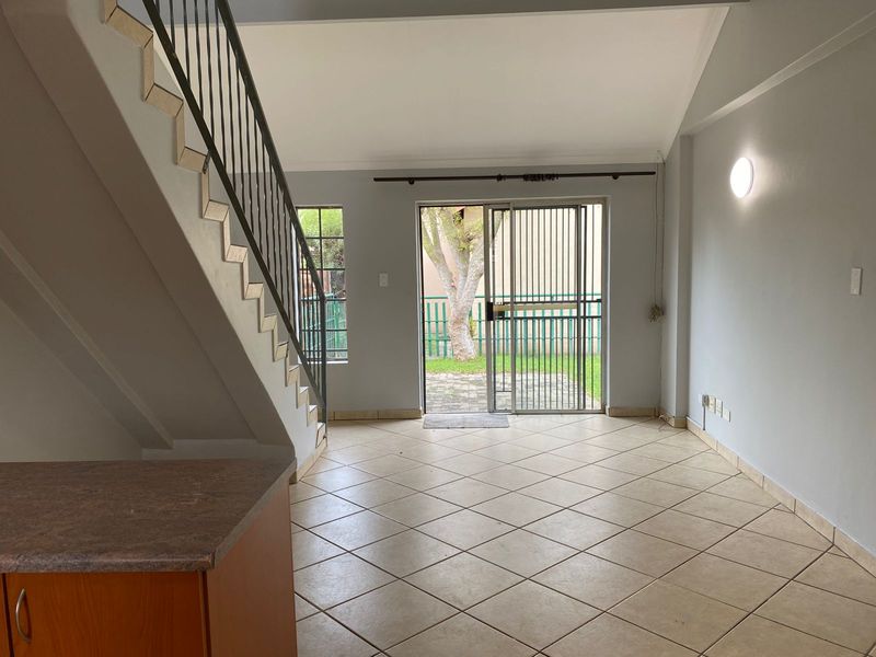 Open-plan living area featuring tiled flooring, a staircase with metal balustrade, and direct access to the rear garden through a sliding glass door.