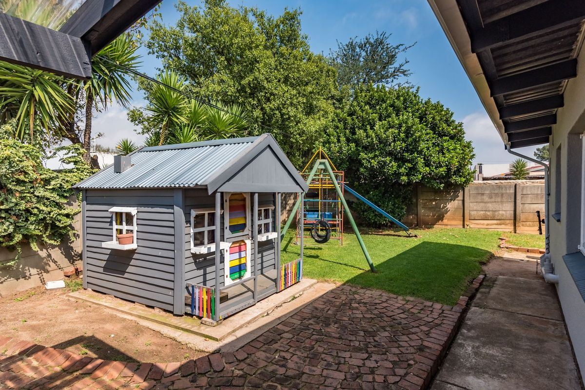A private rear garden featuring a paved walkway, established lawn, and a play area with a wooden playhouse and swing set.