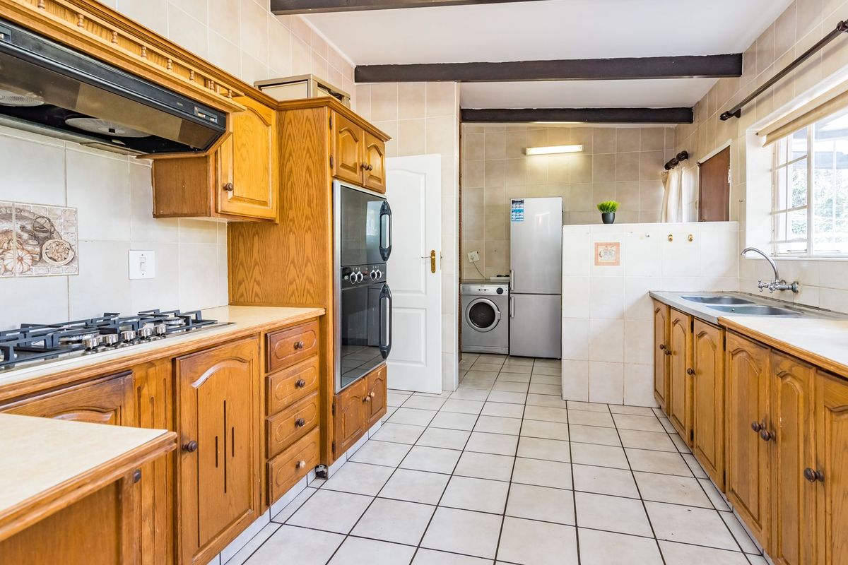 A functional kitchen featuring wooden cabinetry, built-in oven, gas hob, and an adjoining scullery area with tiled flooring throughout.