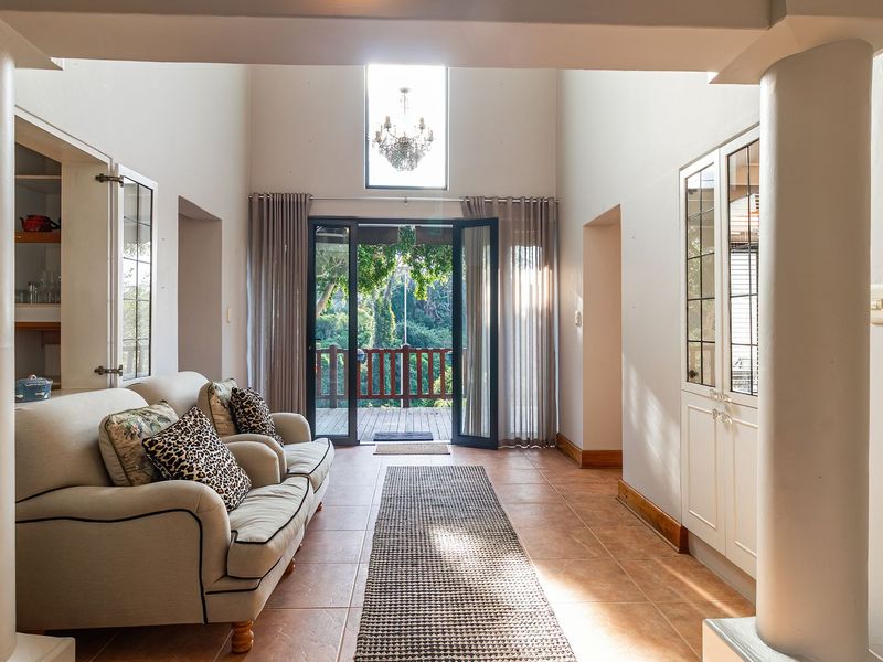Spacious living area featuring high ceilings, tiled flooring, built-in cabinetry, and double doors opening onto a wooden deck with garden views.