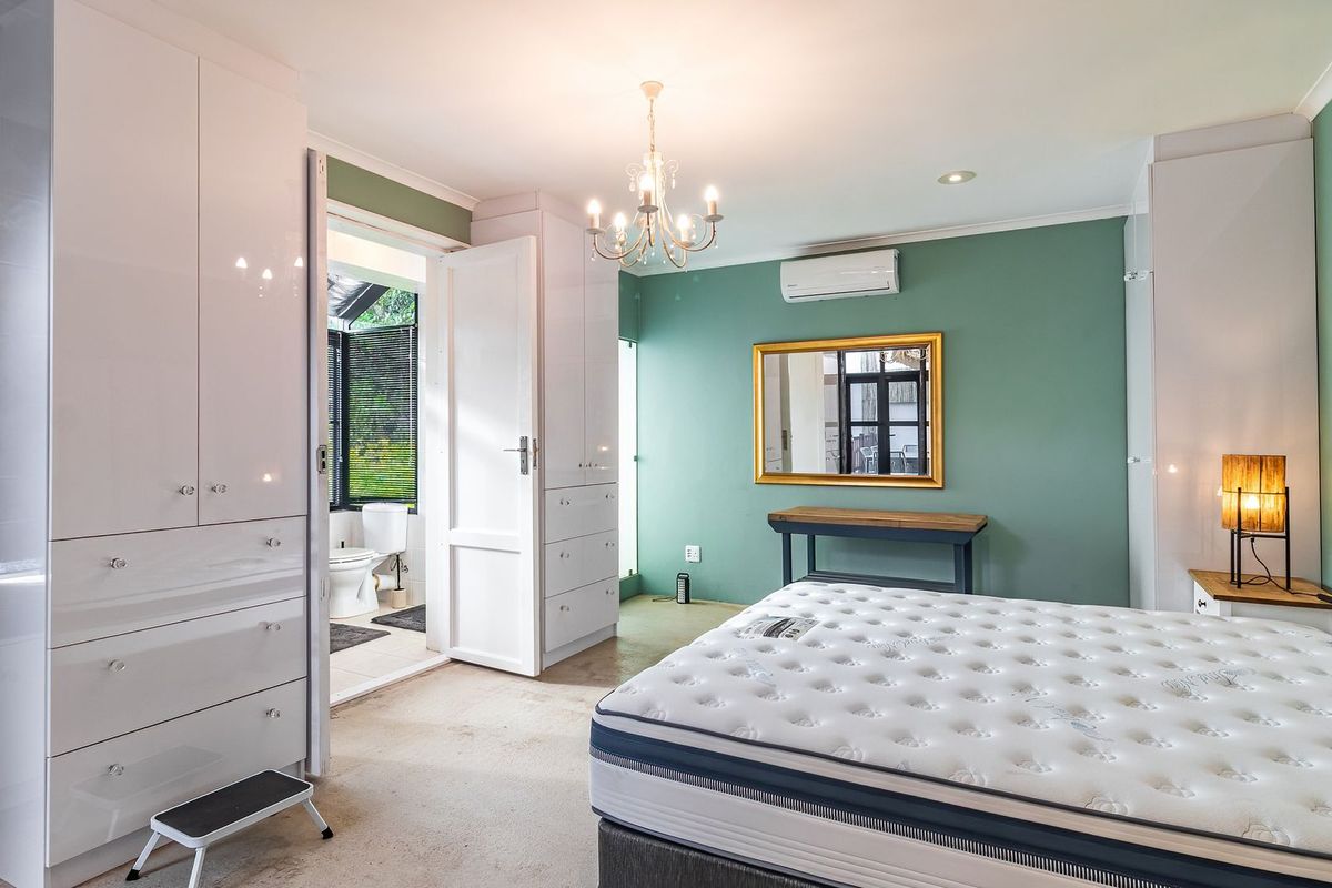 Spacious bedroom featuring built-in high-gloss cabinetry, an en-suite bathroom, and a wall-mounted air conditioning unit.