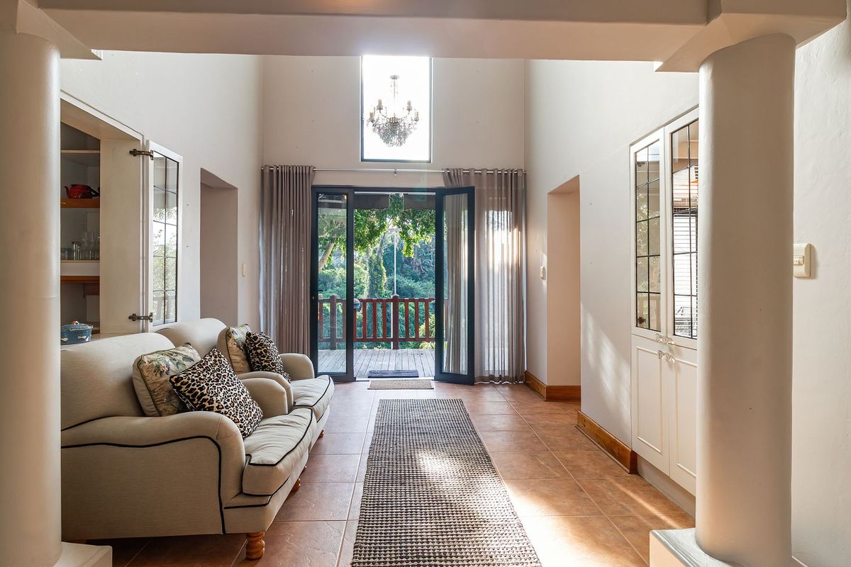 Spacious living area featuring high ceilings, tiled flooring, built-in cabinetry, and double doors opening onto a wooden deck with garden views.