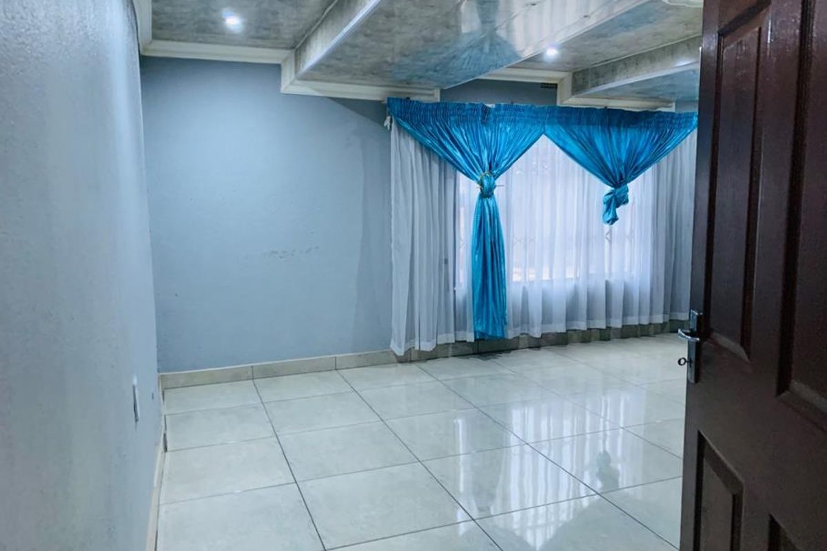 A spacious, empty living room featuring large format floor tiles, recessed ceiling lighting, and a decorative drop ceiling design.