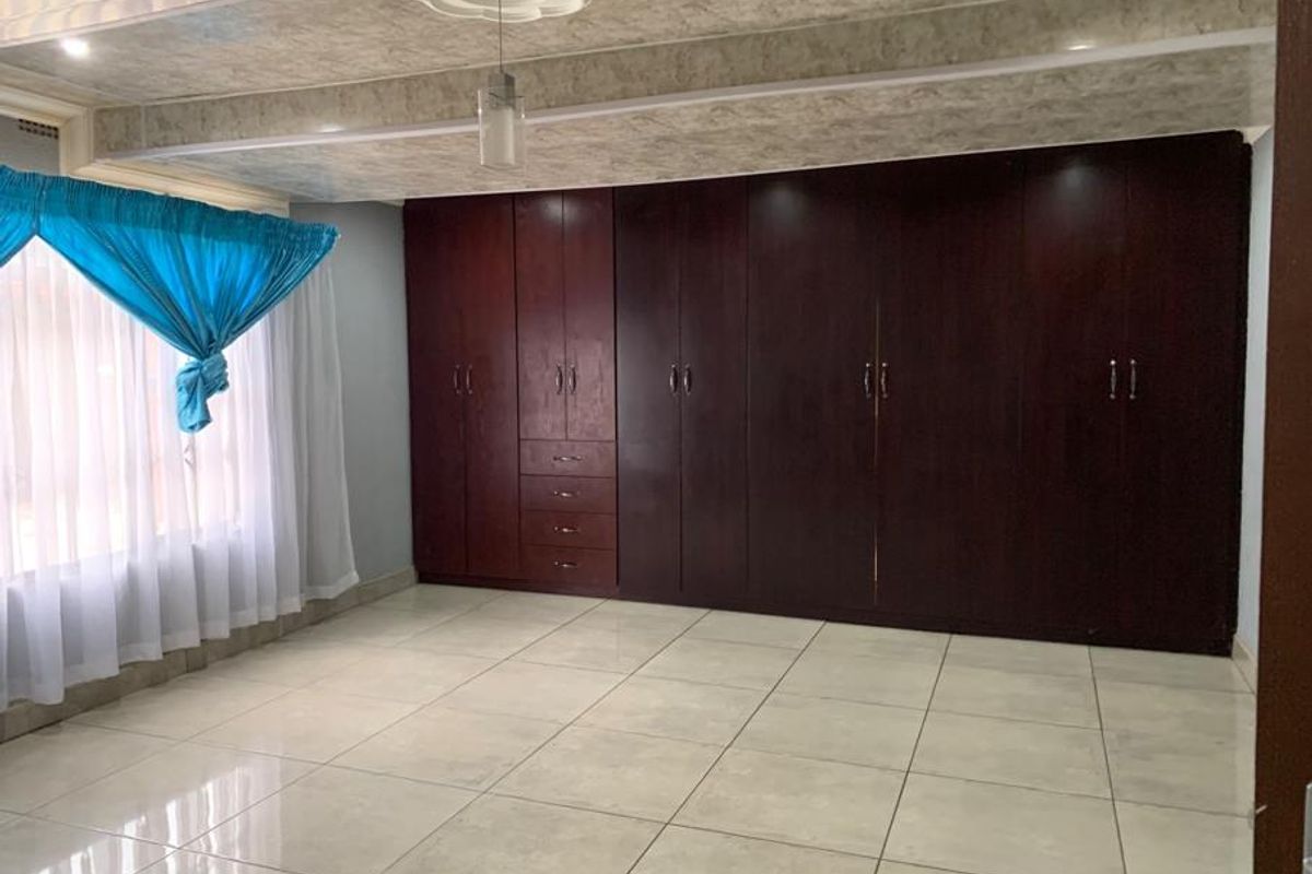 A spacious bedroom featuring extensive built-in dark wood cabinetry, tiled flooring, and a decorative ceiling rose with a pendant light fixture.