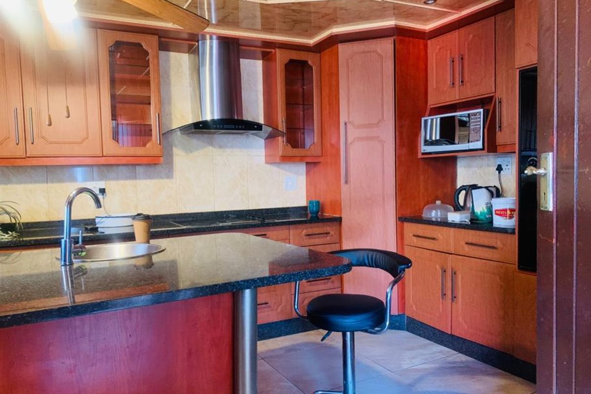 A functional kitchen featuring wood-toned cabinetry, granite countertops, a central island with a breakfast bar, and a stainless steel extractor fan.