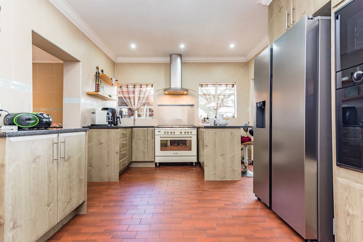 A well-maintained kitchen featuring wood-look cabinetry, a stainless steel extractor fan, a freestanding oven, and terracotta-style tiled flooring.