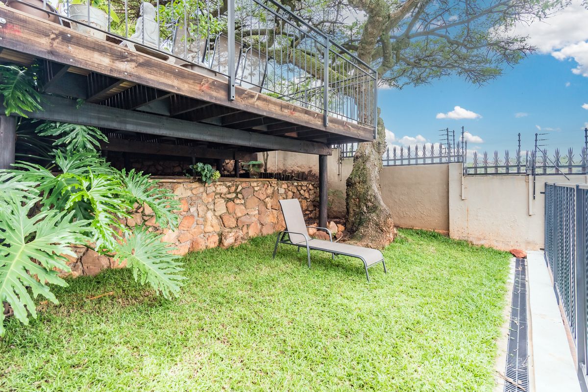 A private rear garden featuring a raised timber deck with metal balustrades, a stone retaining wall, and secure perimeter fencing with electric security wires.