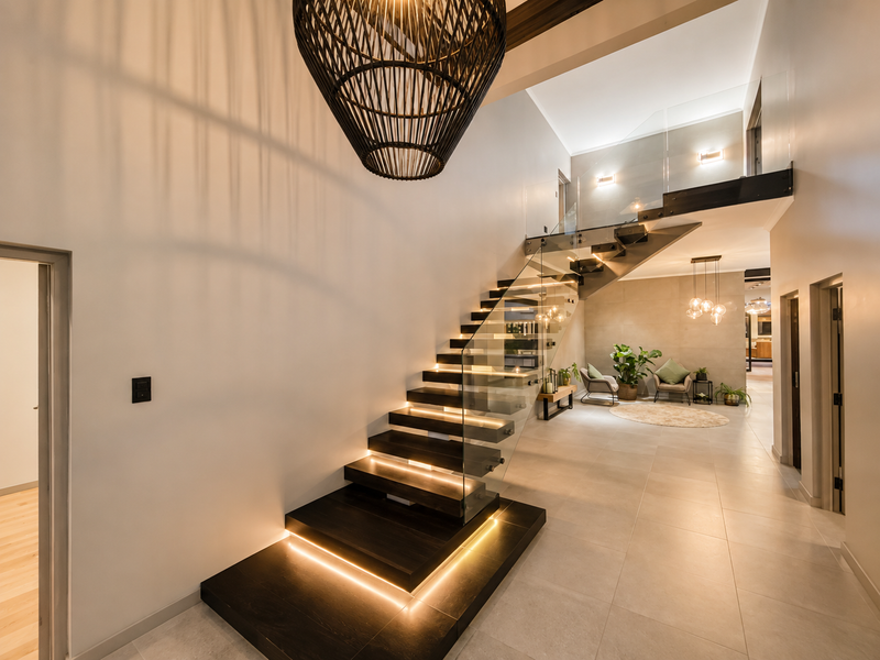 Modern entrance hall featuring a striking floating staircase with glass balustrades, integrated LED lighting, and high-quality tiled flooring.