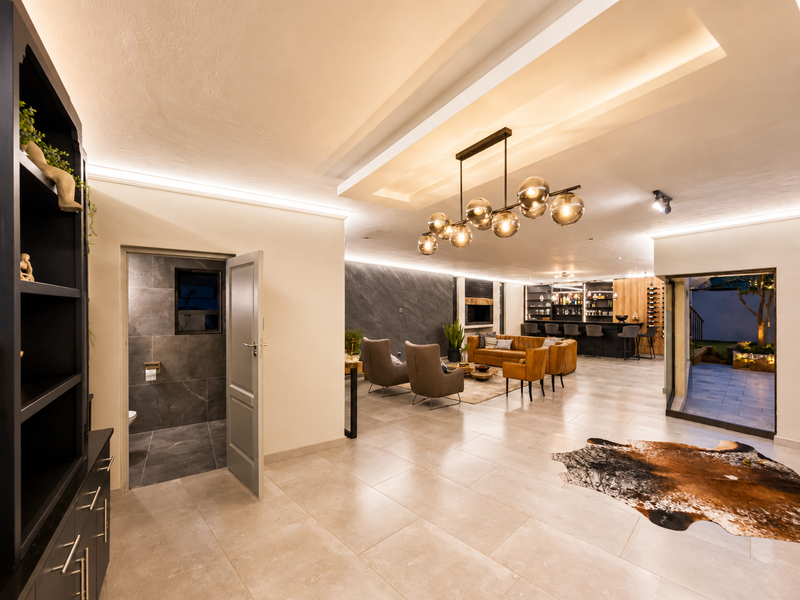 Spacious open-plan living area featuring modern tiled floors, recessed ceiling lighting, a stylish feature pendant, and a sophisticated built-in bar area.