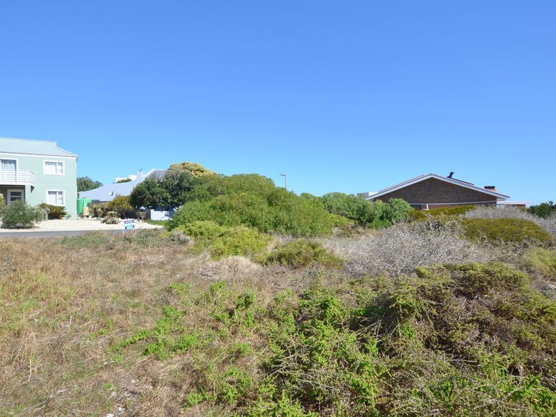 A view of a vacant residential plot featuring natural coastal vegetation with surrounding established residential properties in the background.