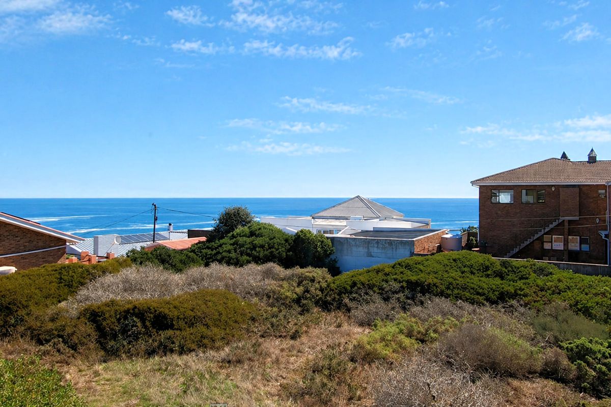 A view of a vacant residential plot featuring natural coastal vegetation with surrounding residential properties and an expansive ocean horizon in the background.