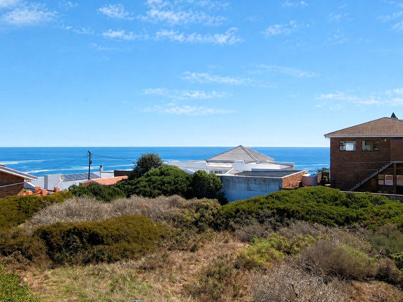 A view of a vacant residential plot featuring natural coastal vegetation with surrounding residential properties and an expansive ocean horizon in the background.