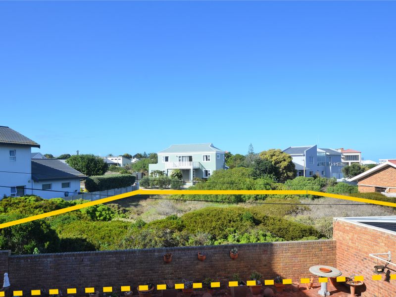An elevated view of a vacant residential plot featuring natural vegetation, bordered by a brick boundary wall and surrounding suburban homes.