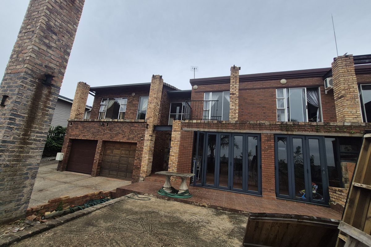 Rear exterior view of a multi-story brick house featuring a tiled patio, large folding glass doors, and multiple chimneys.
